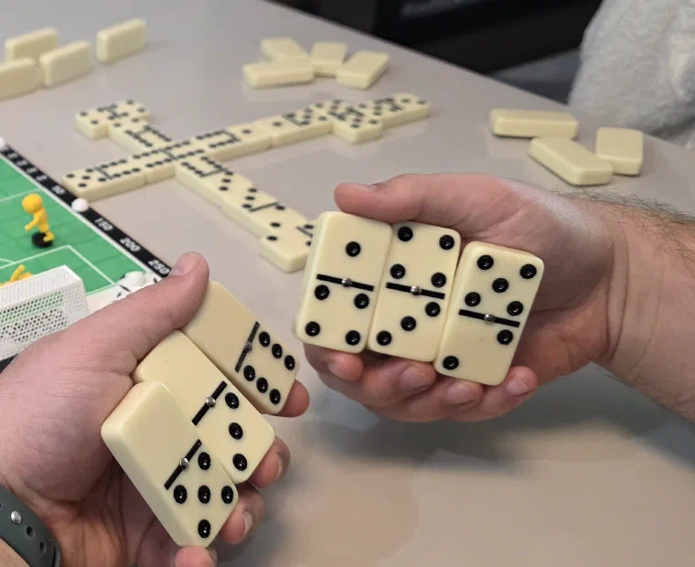 Dois jogadores segurando peças de dominó ao redor do tabuleiro do Domino Futebol Clube